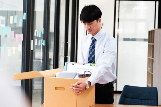 A man in a suit is opening a cardboard box on a desk. The box contains papers and a laptop