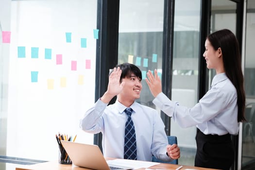Two elated business colleagues giving a high-five over a successful project at their office workspace.