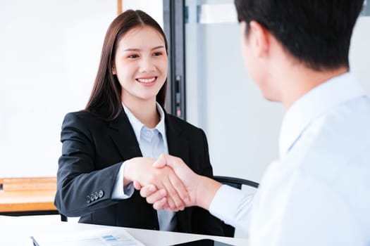 A young businesswoman smiles while shaking hands, making a positive impression during a professional meeting.