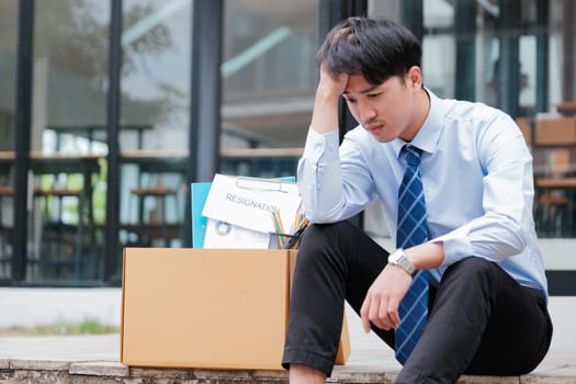 Disheartened Man Sitting on Stairs with Box of Personal Items, Overwhelmed by Emotions After Resignation or Job Loss