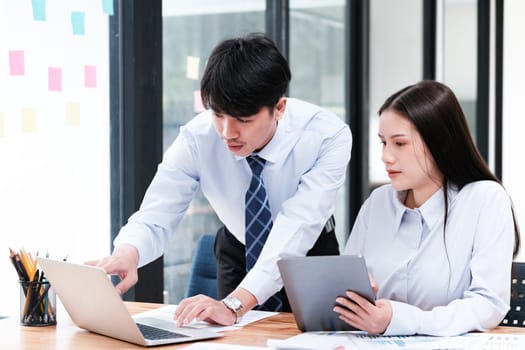 Asian business colleagues in discussion over digital and paper data analysis for company growth strategy at an office desk.