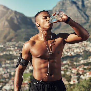 Black man, shirtless and drink water in outdoors for running, thirst and hydrate on sport break. Person, mountain and mineral liquid in bottle for nutrition, music and phone app for streaming song.