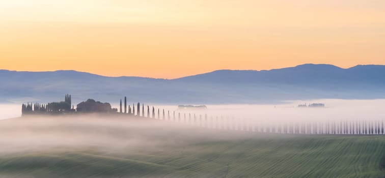 Pienza, Tuscany, Italy – April 13, 2024: House surrounded by cypress trees among the misty morning sun-drenched hills of the Val d'Orcia valley at sunrise in San Quirico d'Orcia, Tuscany, Italy