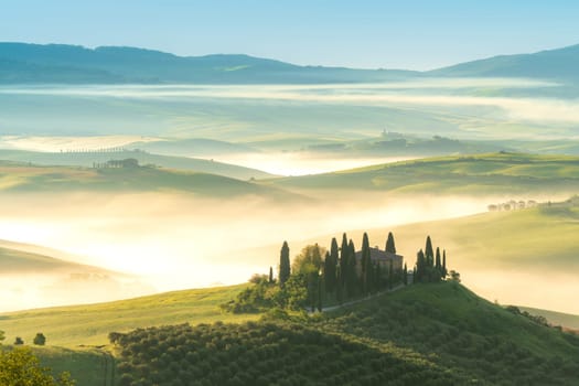 Pienza, Tuscany, Italy – April 13, 2024: House surrounded by cypress trees among the misty morning sun-drenched hills of the Val d'Orcia valley at sunrise in San Quirico d'Orcia, Tuscany, Italy