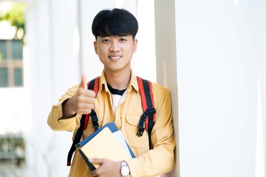 A young man is holding a stack of books and giving a thumbs up. He is smiling and he is happy