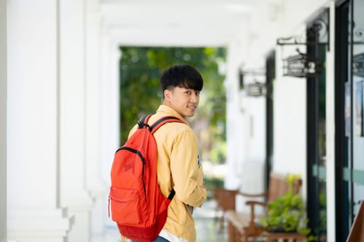 A college student stands in the hallway of his school, holding textbooks and smiling, ready for a day of learning and studies.