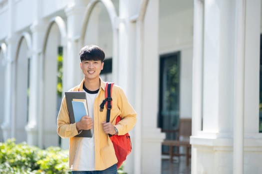 A contented college student carrying a laptop and books walks across the campus grounds, exuding a sense of readiness and enthusiasm for learning.