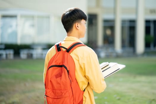 A university student stands thoughtfully on campus, gazing into the distance with his books in hand, ready for a day of studies.