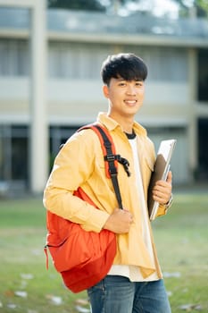 A contented college student carrying a laptop and books walks across the campus grounds, exuding a sense of readiness and enthusiasm for learning.