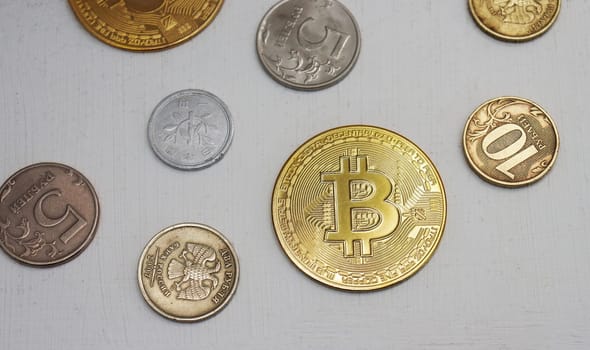 Yellow bitcoin coin, 1 and 5 Russian ruble coins on a light gray background, top view.