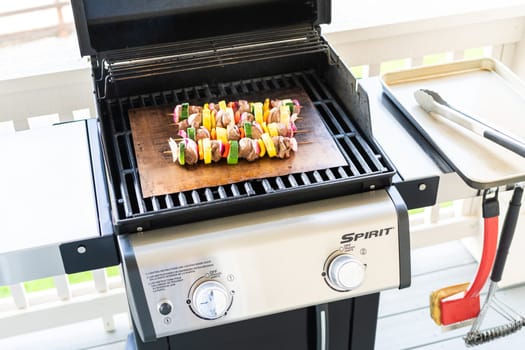 Skewered beef and fresh veggies sizzle on a copper grill mat over a gas outdoor grill.