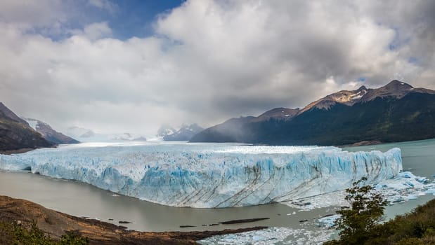 Vast glacier amid mountains under a striking cloudy sky.