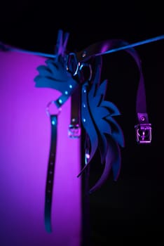 bdsm leather shoulder straps in the shape of wings hanging on clothesline in neon light on a black background, conceptual photos