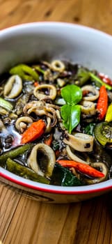 Indonesian home cooking menu, sauteed squid with black ink sauce with spicy seasoning called Tumis Cumi Hitam, including chili, ginger, and lime leaf served in a bowl