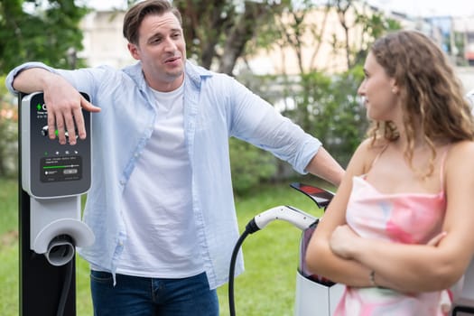 Happy and lovely couple with eco-friendly conscious recharging electric vehicle from EV charging station. EV car technology utilized as alternative transportation for future sustainability. Synchronos