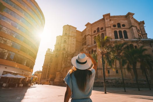 Rear view of young tourist woman in white sun hat walking in Malaga city at sunset. Summer holiday vacation in Spain. High quality photo