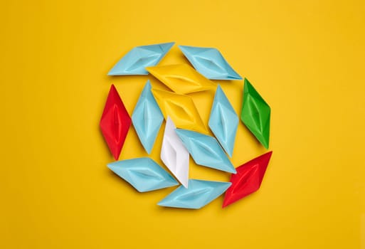 A group of colorful paper boats clustered on a yellow background, top view