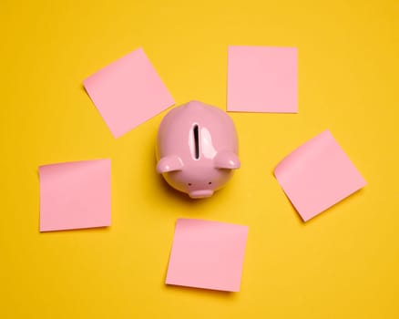 Pink ceramic piggy bank and paper stickers on a yellow background, top view