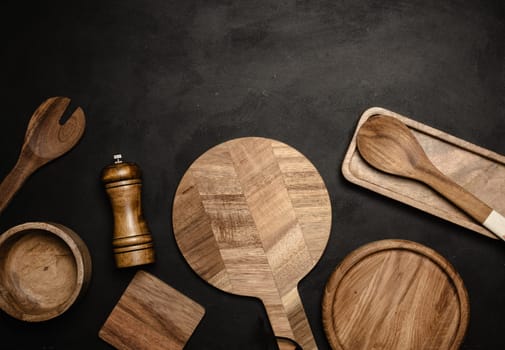 Various wooden kitchen utensils on black background, top view. Copy space
