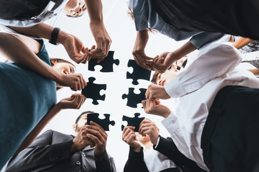 Below view of diverse corporate officer workers collaborate in office connecting puzzle pieces as partnership and teamwork concept. Unity and synergy in business idea by merging jigsaw puzzle. Concord