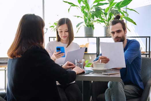 Couple of young clients at meeting with agent broker insurer realtor seller reading paper contract. Family customers tenants financing investment insurance rental offer, conclusion of purchase sale