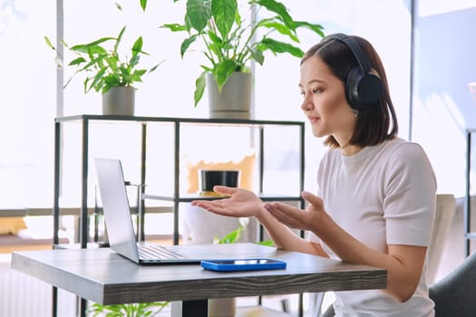 Young woman in headphones having video chat conference call using laptop computer sitting in cafe. Female university college student studying online listening webinar preparing exam, working remotely