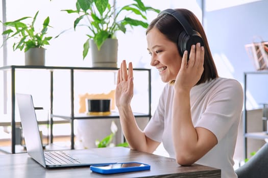 Young woman in headphones having work video chat conference call, using laptop computer, sitting in cafe coworking. Remote virtual online work, study, freelance, blog vlog, internet technology youth