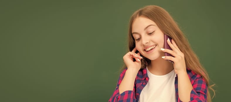 happy kid speaking on smartphone in classroom at blackboard, copy space, conversation. Horizontal isolated poster of school girl student. Banner header portrait of schoolgirl copy space