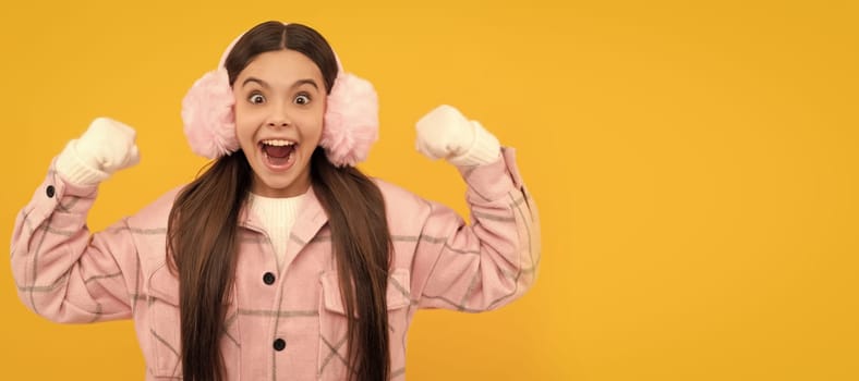 Winter girl. amazed kid in winter mittens and earmuffs on yellow background, winter fashion. Banner of christmas child girl, studio kid winter portrait with copy space