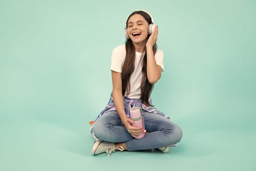 Teen girl in headphones listen to music. Wireless headset device accessory. Child enjoys the music in earphones on blue background