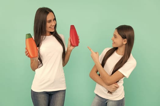 happy mother and daughter hold shampoo bottle on blue background. point finger.