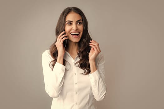 Excited amazed charming brunette woman talking on mobile phone, isolated over gray background. Girl with mobile cell phone