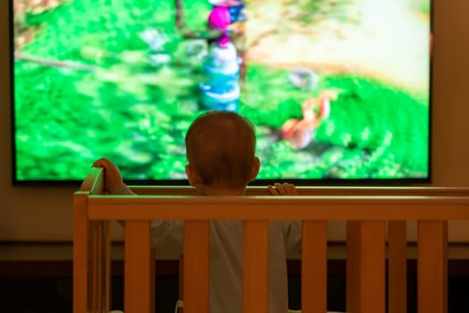 The baby watches a large TV from a crib. Concept of knowledge.