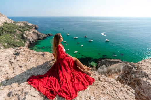 Woman red dress sea. Happy woman in a red dress and white bikini sitting on a rocky outcrop, gazing out at the sea with boats and yachts in the background