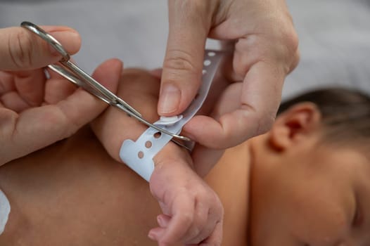 A woman cuts a tag from a newborn boy's hand with nail scissors. Close-up of hands