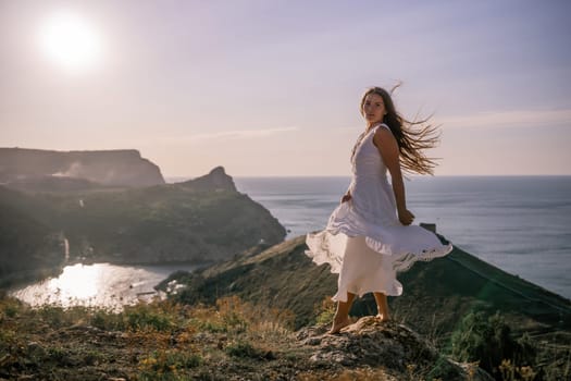 A woman stands on a hill overlooking the ocean. She is wearing a white dress and has long hair. The scene is serene and peaceful, with the sun shining brightly in the background