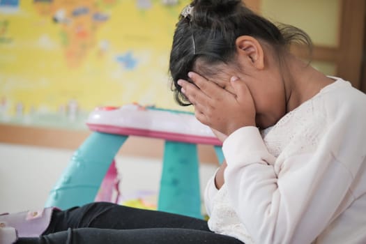 a upset child girl cover her face with hand .