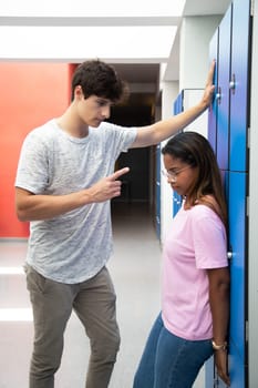 Submissive black teen female high school student victim of abusive relationship with boyfriend.Male teen intimidating girlfriend in high school corridor. Vertical. Adolescent toxic relationship.