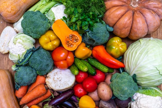 Various vegetables are laid out on a wooden table. Large assortment of vegetables food. pumpkin cabbage broccoli pepper tomatoes carrots and others.