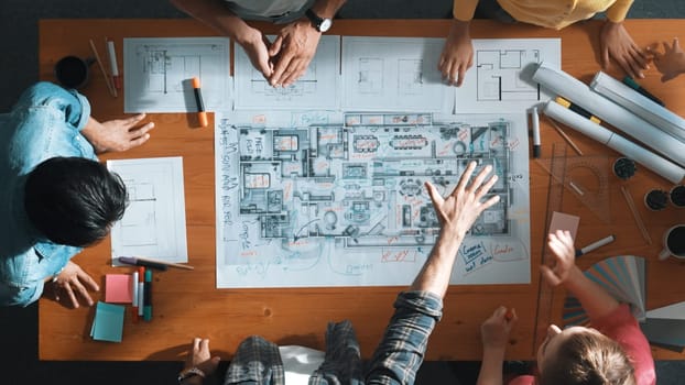 Top view of civil engineer team holding blueprint and standing at table with laptop, project plan and blueprint. Aerial view of skilled project manager planning and writing on sticky notes. Symposium.