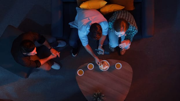 Family and colleague sitting at dark living room with red filter while cheering football team together. Caucasian people enjoy watching tv and giving high five to celebrate winning team. Convocation.