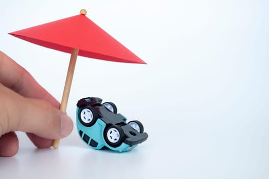 Red toy umbrella and upside down car on white background. Car insurance concept.