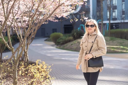 Blonde touches a branch of blooming cherry standing in the park. High quality photo