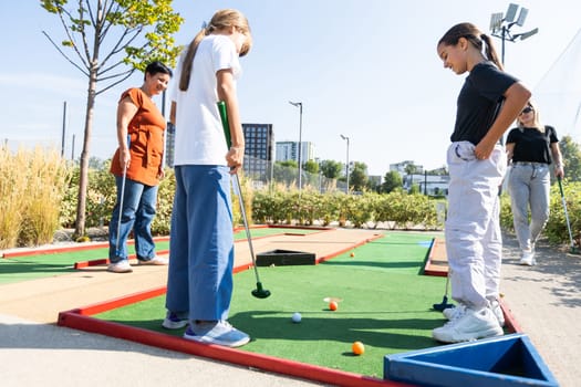 Cute school girl playing mini golf with family. Happy toddler child having fun with outdoor activity. Summer sport for children and adults, outdoors. Family vacations or resort. High quality photo