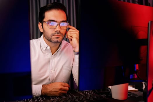 Smart businessman wearing glasses, concentrating on dynamic stock exchange investment on two pc screens at neon light office in dark room night with high profit in searching research market. Surmise.