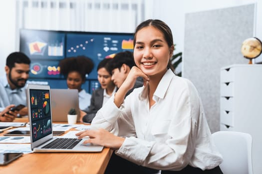 Portrait of happy young asian businesswoman with group of office worker on meeting with screen display business dashboard in background. Confident office lady at team meeting. Concord