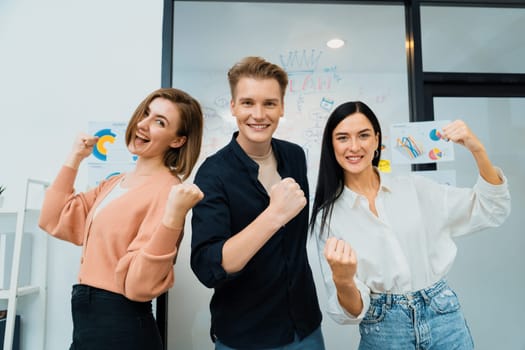 Successful caucasian business team posing victory pose to celebrate successful idea at creative business meeting in front of glass board. Unity and teamwork concept. Immaculate.