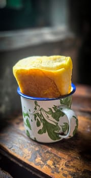 Ice chocolate drink on a vintage Indonesian iron mug with random green pattern called Blirik cup or cangkir Blirik on bokeh background along with chocolate filling bread on a cafe in Bogor