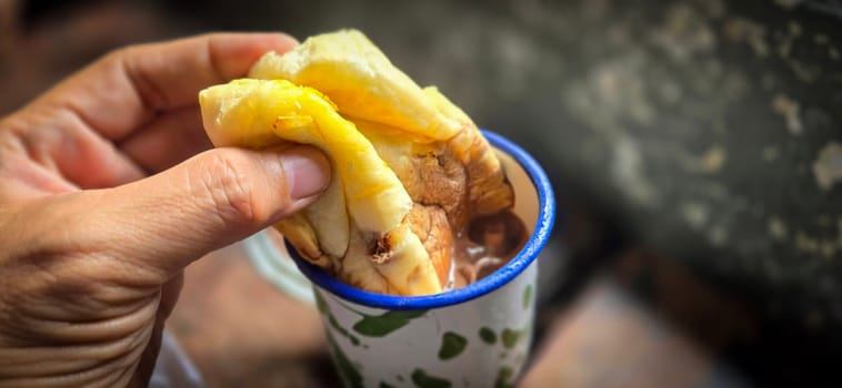 Ice chocolate drink on a vintage Indonesian iron mug with random green pattern called Blirik cup or cangkir Blirik on bokeh background along with chocolate filling bread on a cafe in Bogor