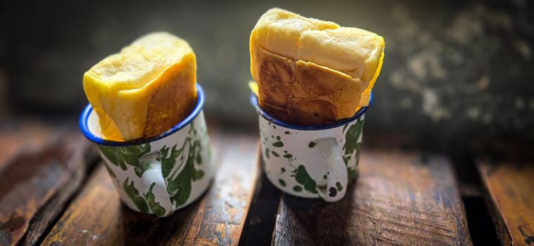 Ice chocolate drink on a vintage Indonesian iron mug with random green pattern called Blirik cup or cangkir Blirik on bokeh background along with chocolate filling bread on a cafe in Bogor